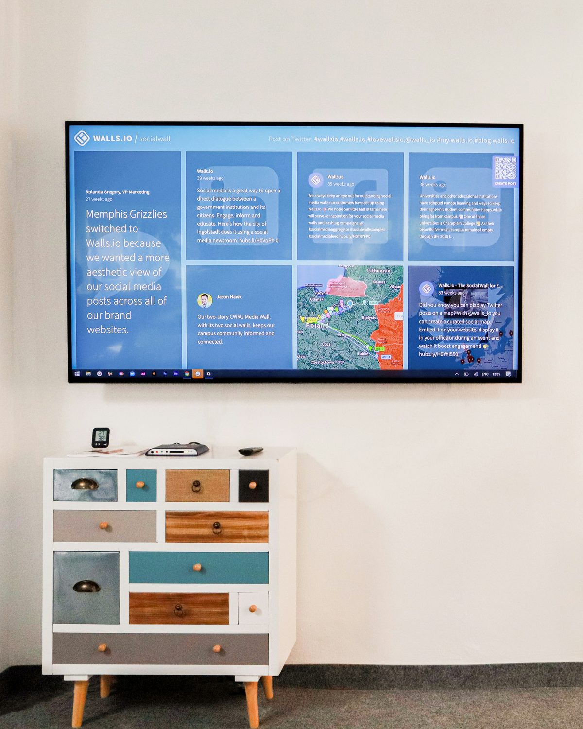 A wall-mounted digital signage display showing a live social wall in an office