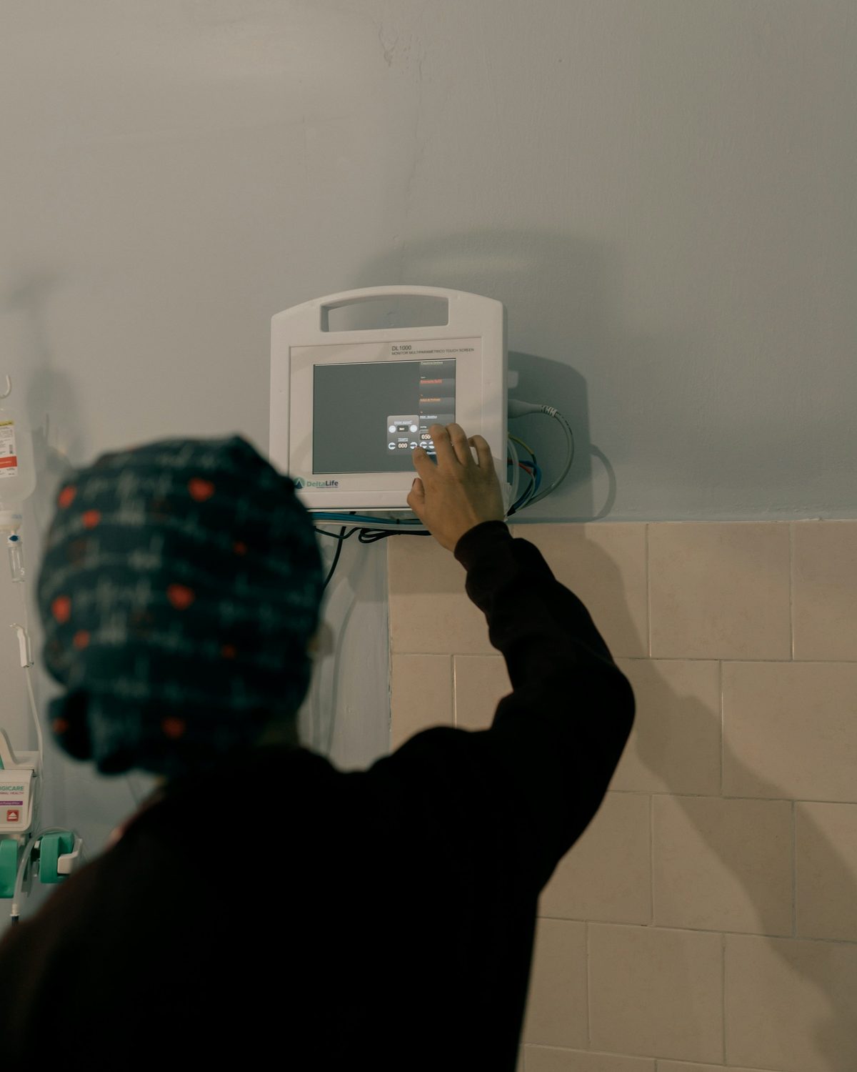 A healthcare worker operating a wall-mounted patient monitor